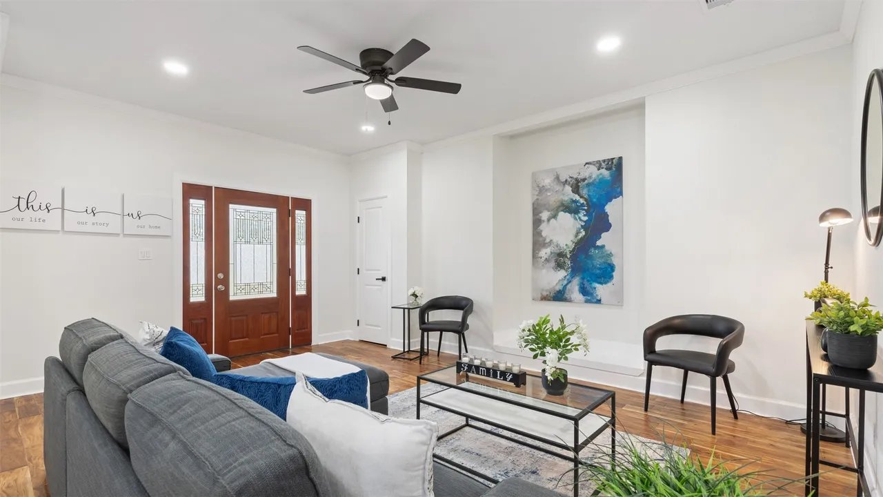 Living room facing the wood front door with leaded-glass sidelights, ceiling fan, and crown molding