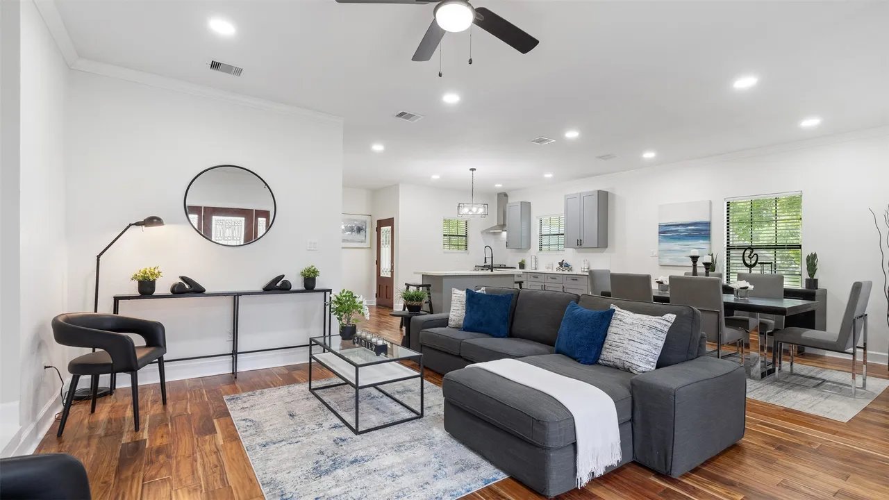 Living room toward the kitchen — gray sectional, large round mirror, and engineered hardwood floors