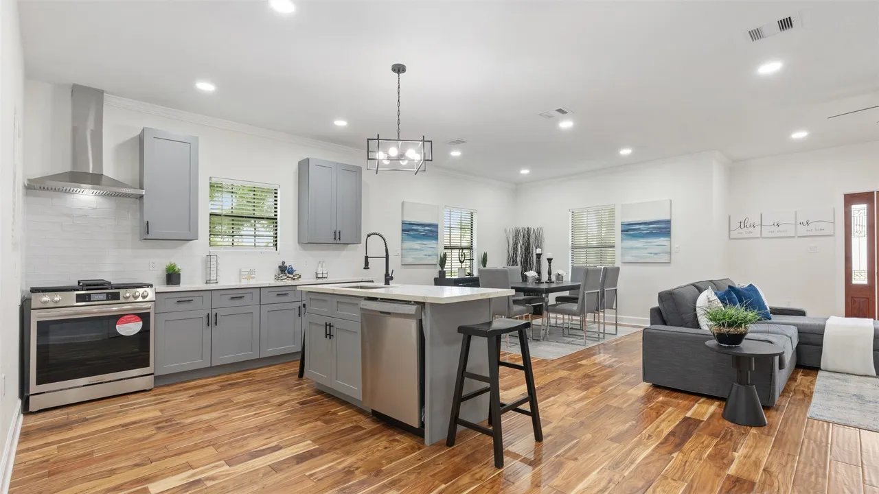 Open kitchen with gray shaker cabinets, quartz island, gas range with chimney hood, and engineered hardwood floors