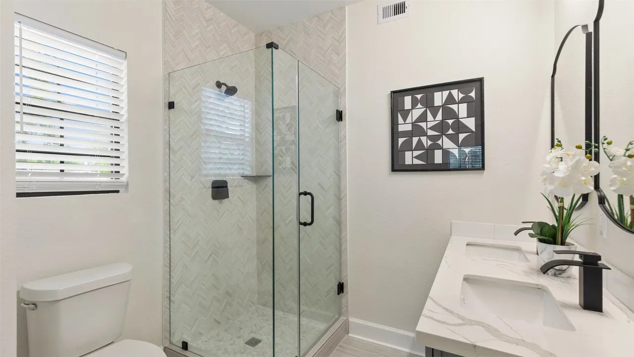 Second bathroom with glass-enclosed walk-in shower in herringbone tile, double vanity