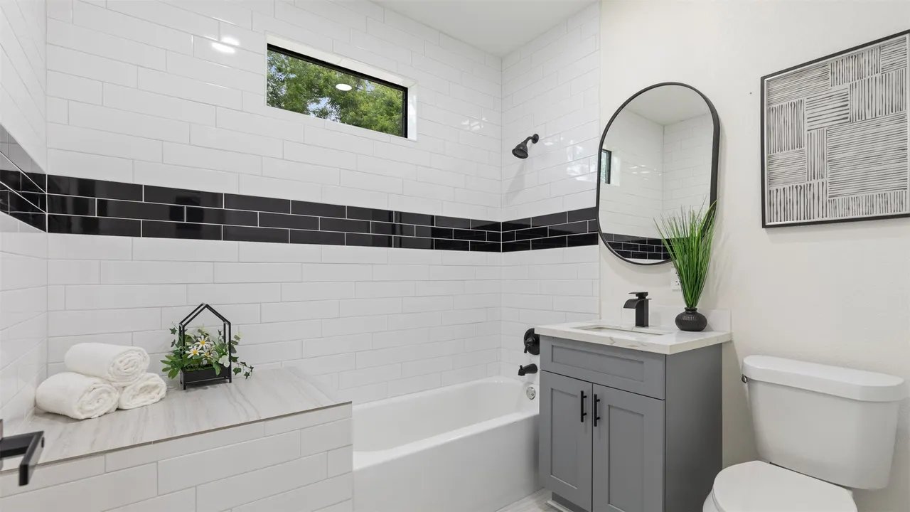 Third bathroom with white subway tile, black accent stripe, and tub/shower combo